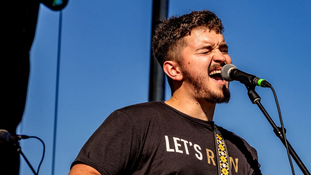 Nic Hitchens singing into a microphone on an outdoor stage.
